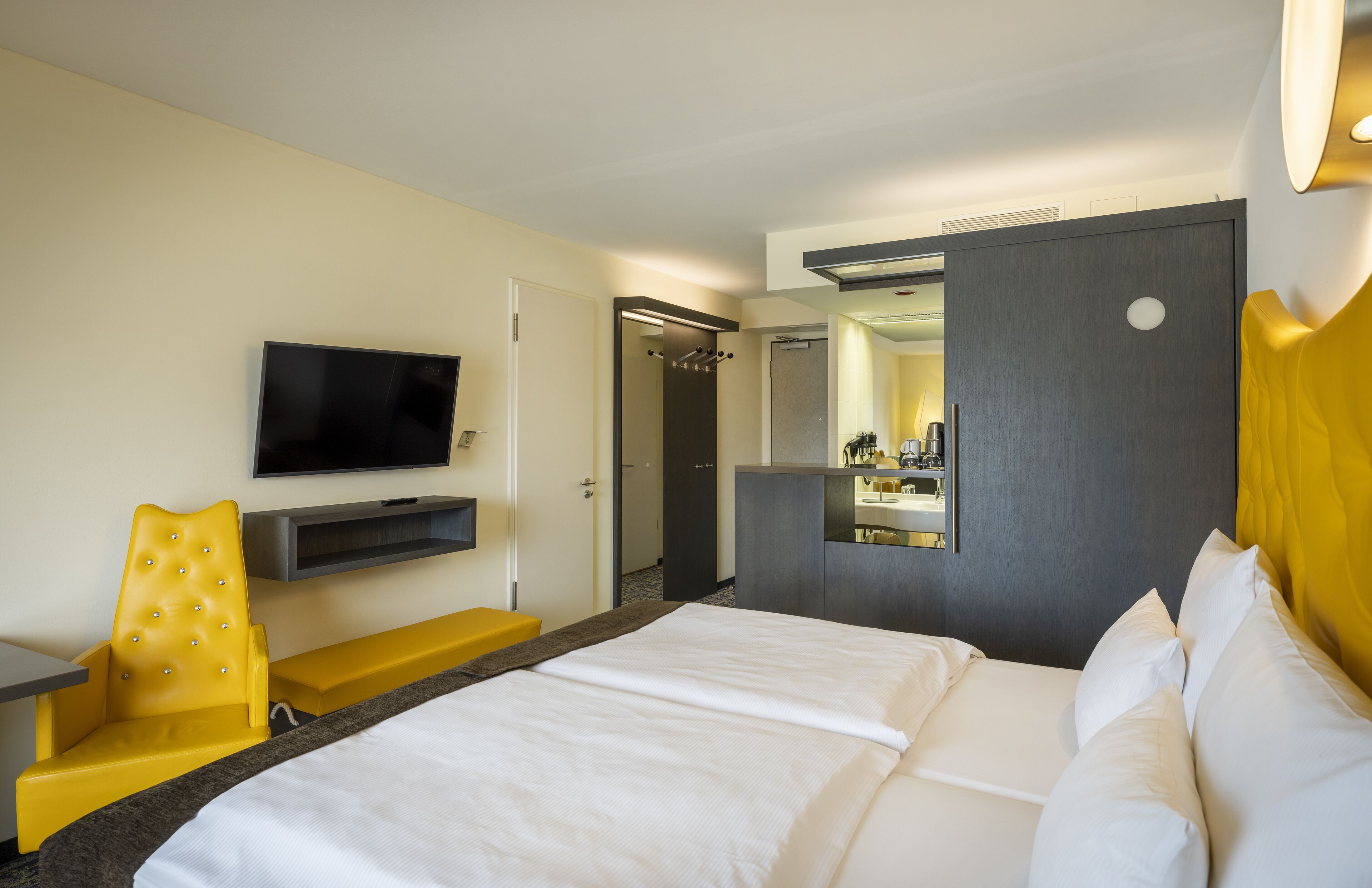 A hotel room with a bed, a TV, a mirror, a chair, and a desk.