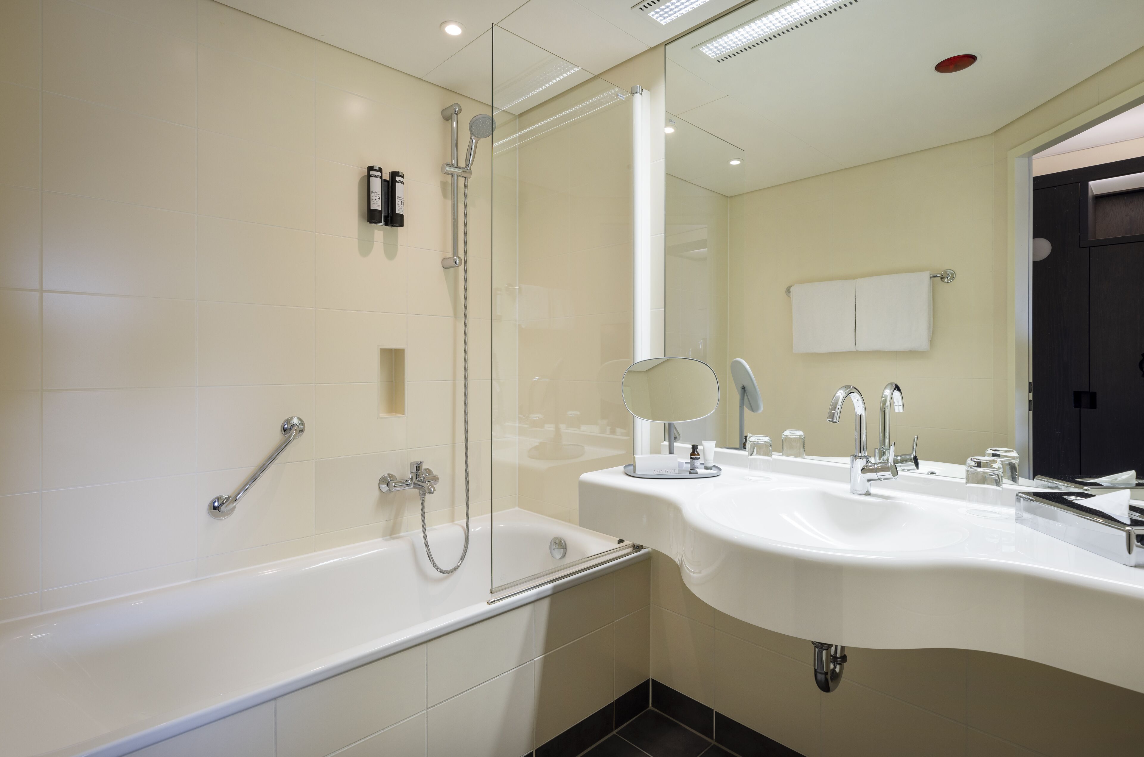 Un baño moderno con ducha de vidrio, tocador con doble lavamanos y un espejo grande.