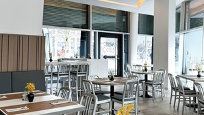 A modern restaurant interior with high ceilings, large windows, and a clean, minimalist design.