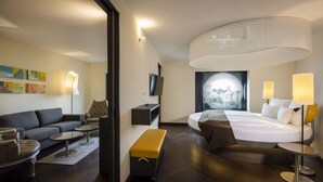 A modern hotel room with a curved ceiling, a large bed, a sofa, a coffee table, a bench, and a TV.