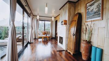 A spacious room with a wooden floor, a sofa, a dining table, and a large window offering a view of the outdoors.
