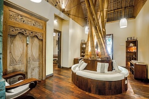 A room with a circular wooden seating area, a wooden door with intricate carvings, and a bamboo ceiling. - Munduk Moding Plantation Nature Resort (Gobleg)