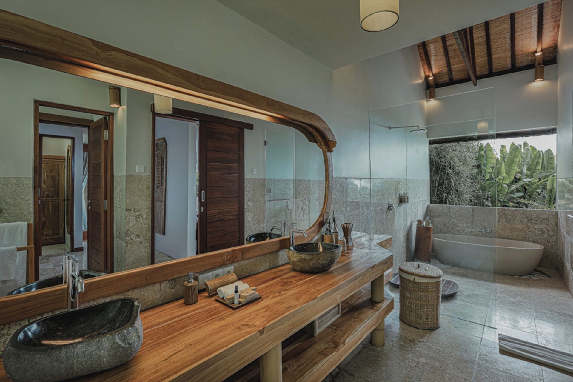 Un bagno con uno specchio grande, un mobile vanitario in legno, un lavabo in pietra e una vasca da bagno.