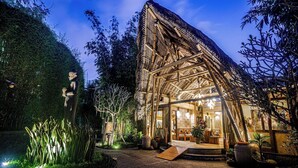A bamboo structure with a glass entrance, surrounded by plants and a statue. - Munduk Moding Plantation Nature Resort (Gobleg)