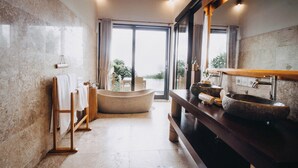 A bathroom with a stone sink, wooden towel racks, and a large window with a view of greenery.