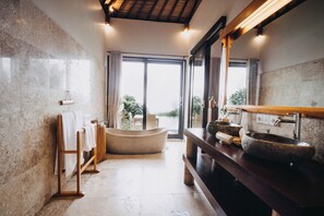A bathroom with a stone sink, wooden towel racks, and a large window with a view of greenery.