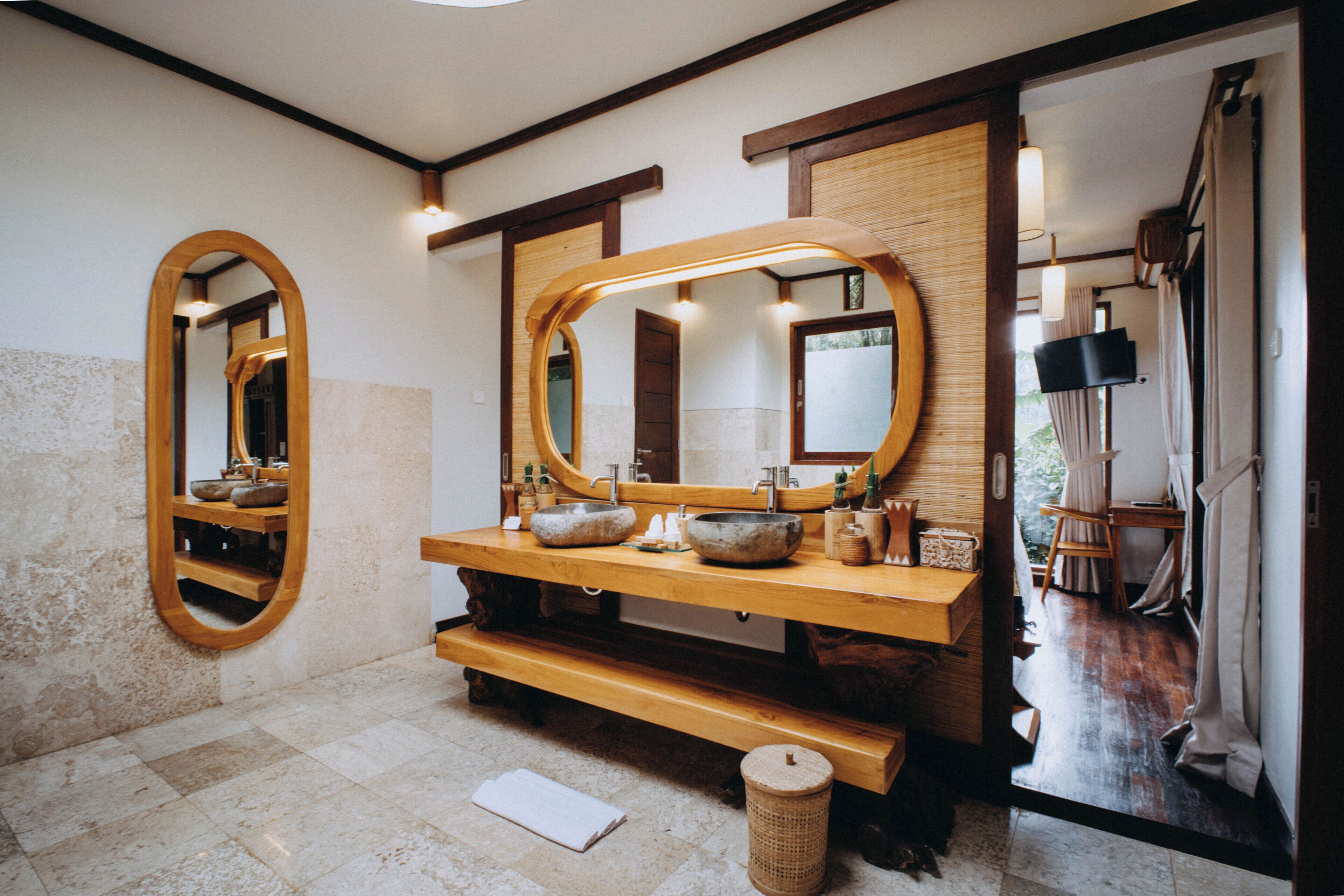 Un baño con tocador de madera, dos espejos grandes y un lavabo con cuenca de piedra.