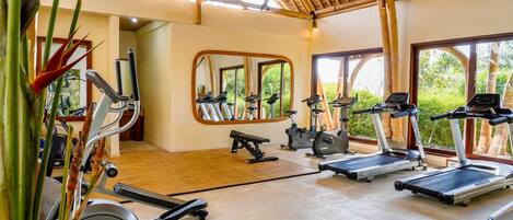 A gym with exercise equipment, large windows, and a bamboo ceiling.