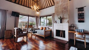 A spacious living room with a wooden floor, a sofa, a chair, and a fireplace. - Munduk Moding Plantation Nature Resort (Gobleg)