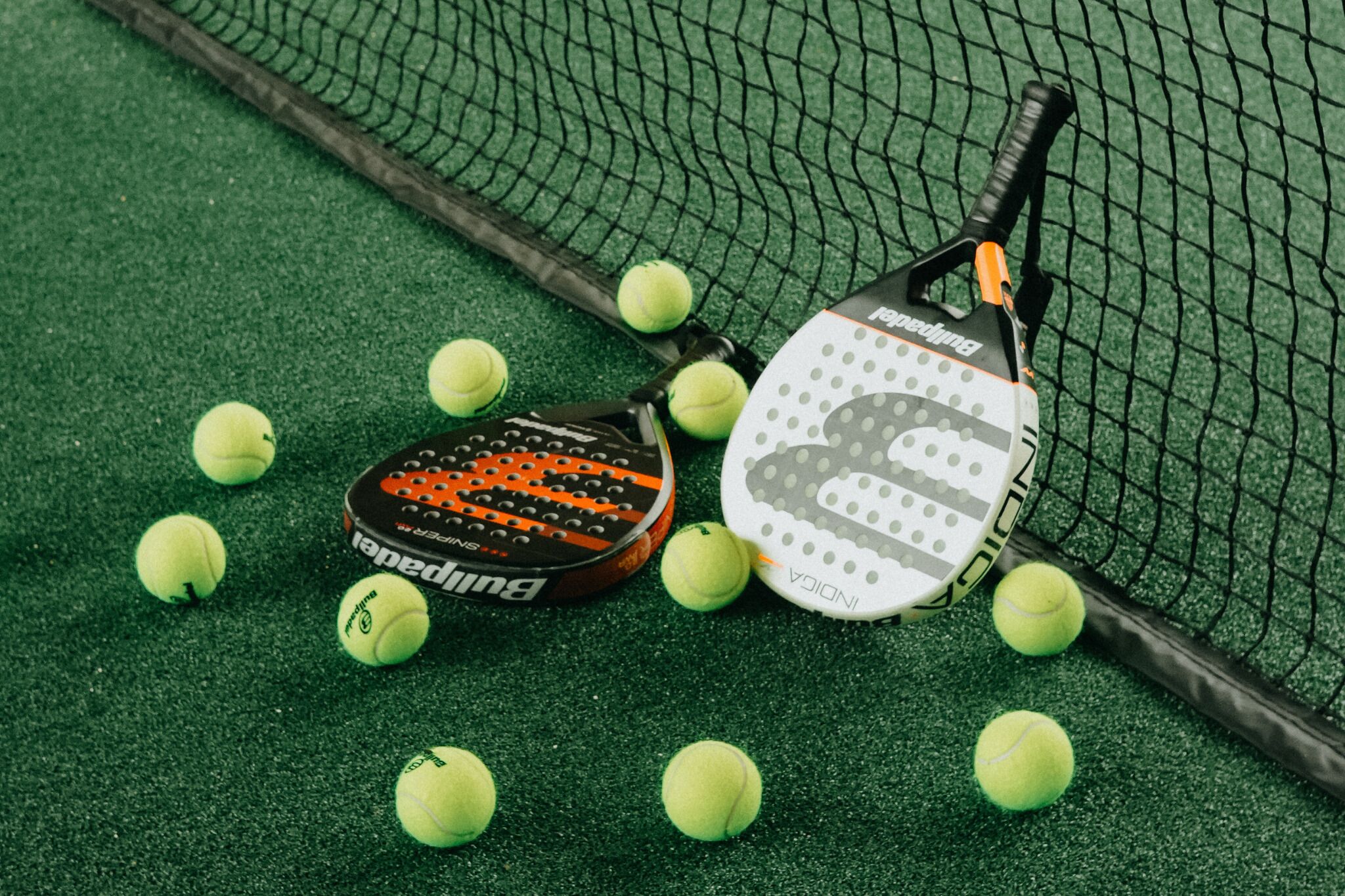 Deux raquettes de tennis sur une surface verte, avec des balles de tennis éparpillées autour.