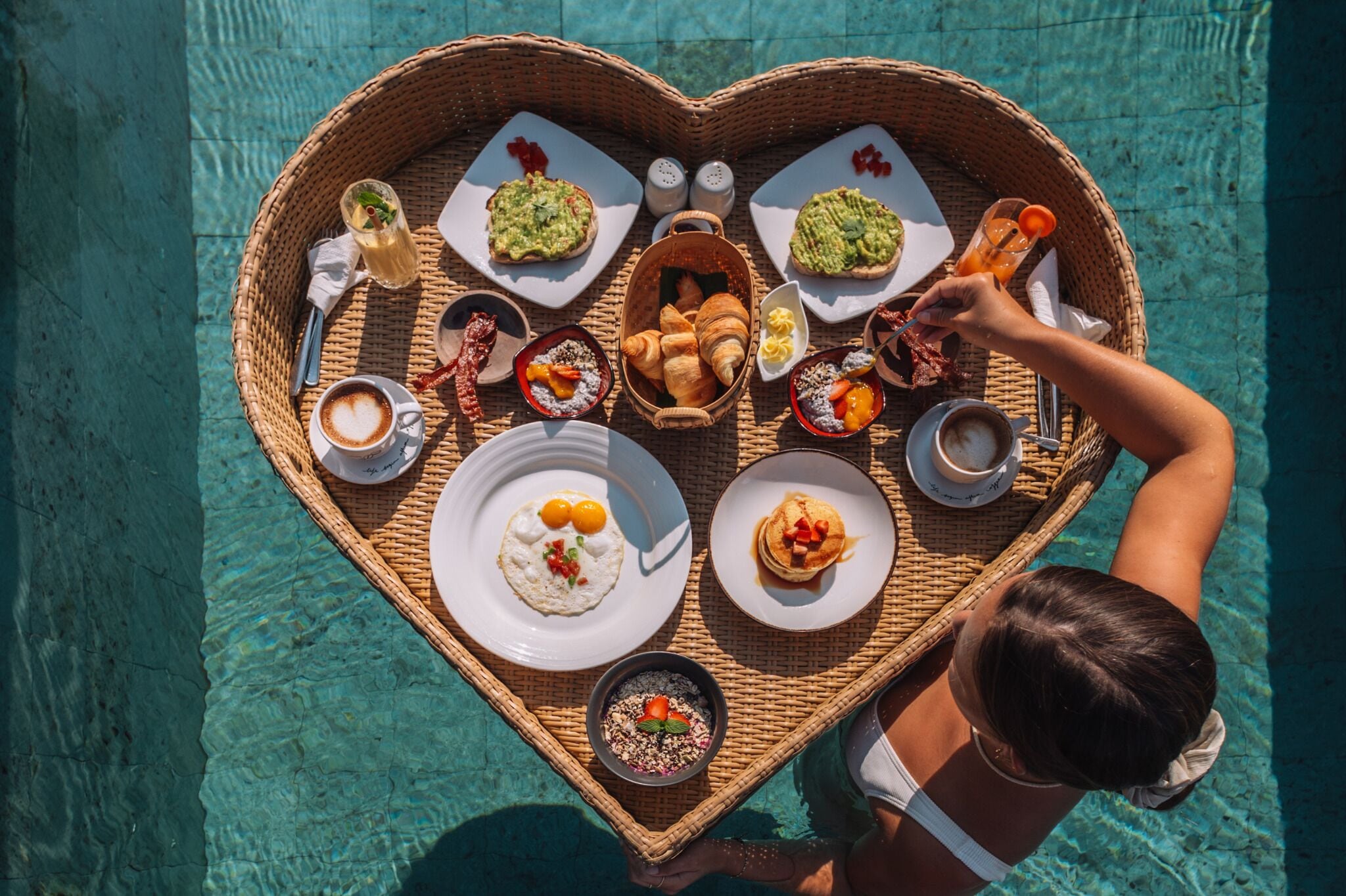 A heart-shaped tray with various breakfast items and drinks, placed on a poolside table.