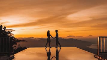 A couple walking on a reflective infinity pool with a sunset view.