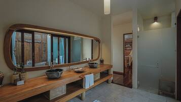 A bathroom with a wooden vanity, a large mirror, a bowl sink, and a shower area.
