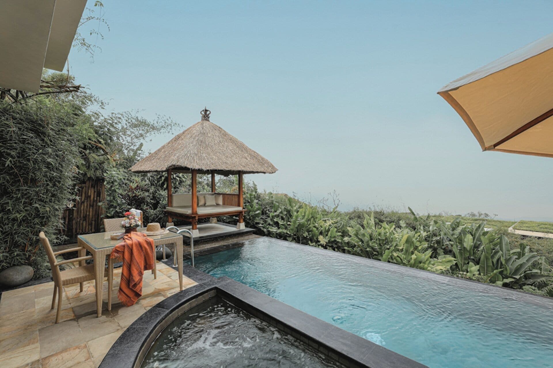 A pool area with a hot tub, a wooden deck, and a thatched-roof structure.