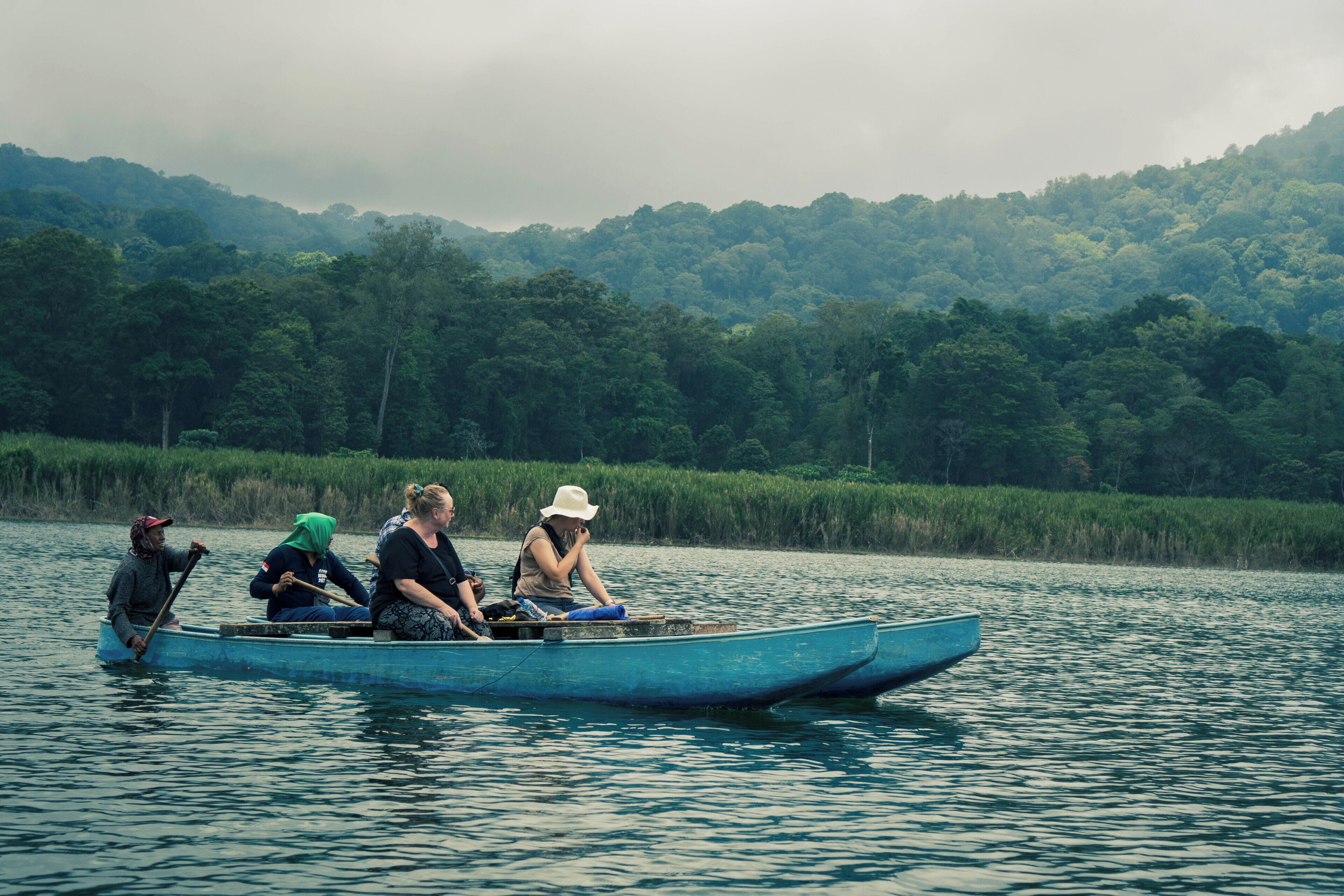 A group of people in a small boat on a body of water with a forested hill in the background.