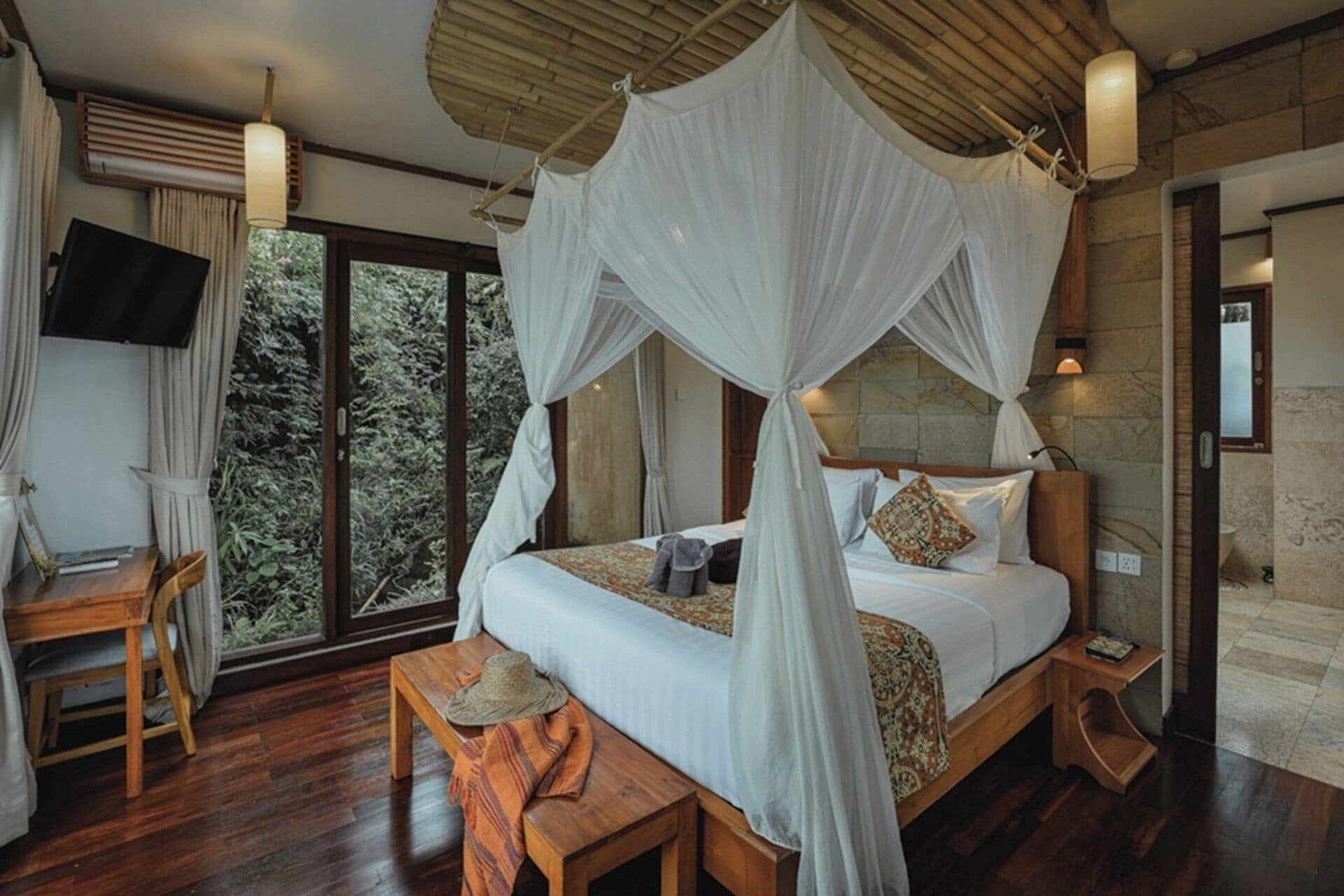 Un dormitorio con cama a dosel, muebles de madera, un televisor y vista a zonas verdes.