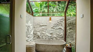 A bathroom with a stone bathtub, a wooden stool, and a woven basket.