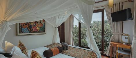 A bedroom with a bed, a television, and a window with a view of greenery.