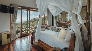 A bedroom with a canopy bed, a television, and a view of the outdoors. - Munduk Moding Plantation Nature Resort (Gobleg)