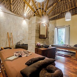 Relax in a serene space with a large bed, a wooden bench, and a stone wall featuring a mirror.