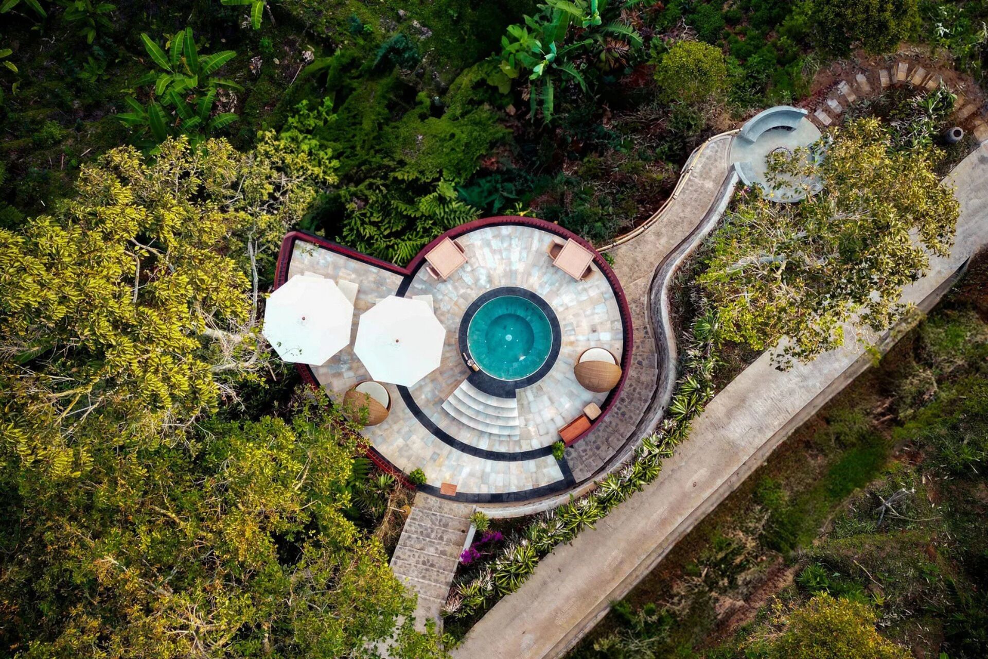 An aerial view of a circular pool with a central fountain, surrounded by a stone deck and seating areas.