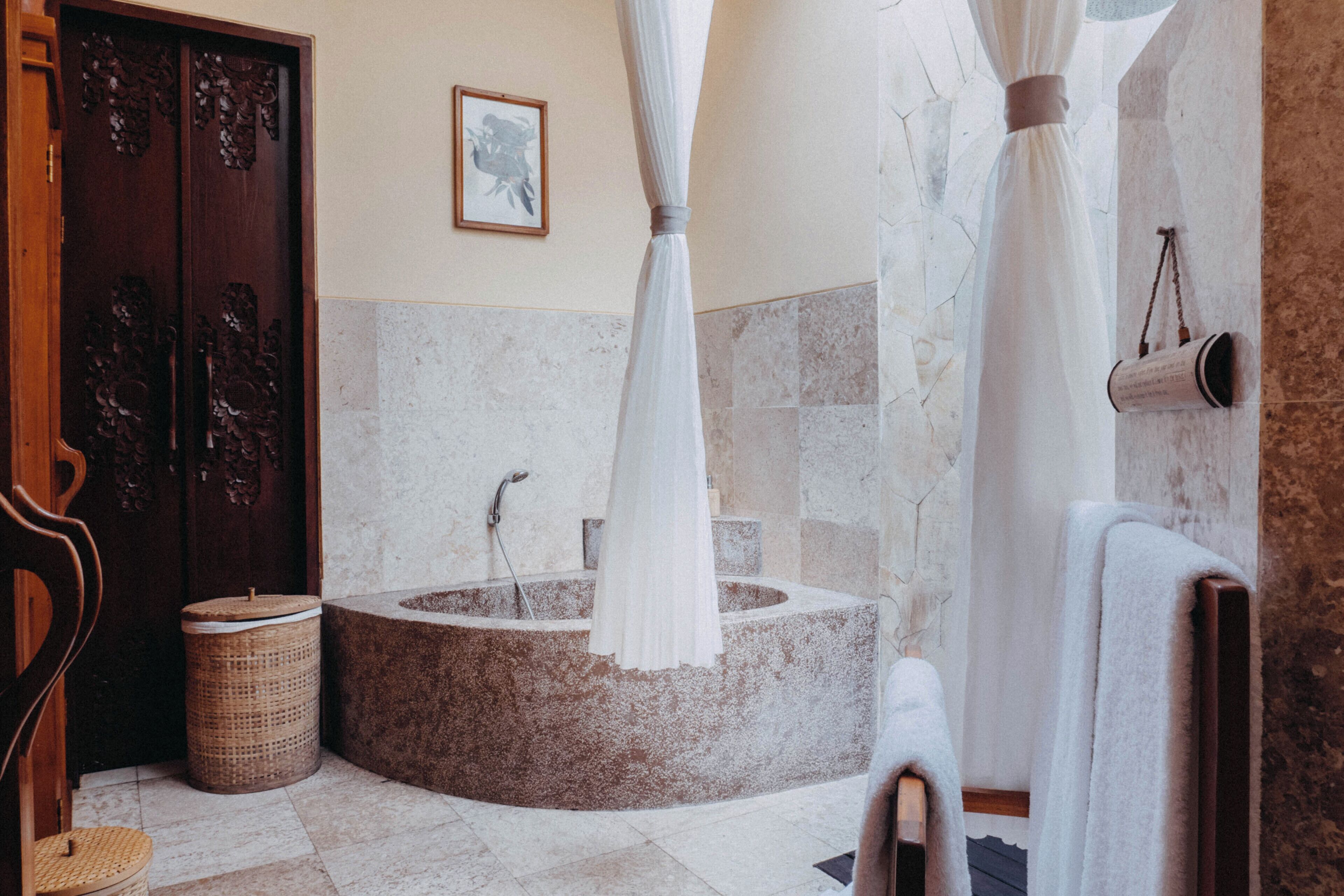 A bathroom with a stone bathtub, a wooden door, a wicker basket, and a towel rack.