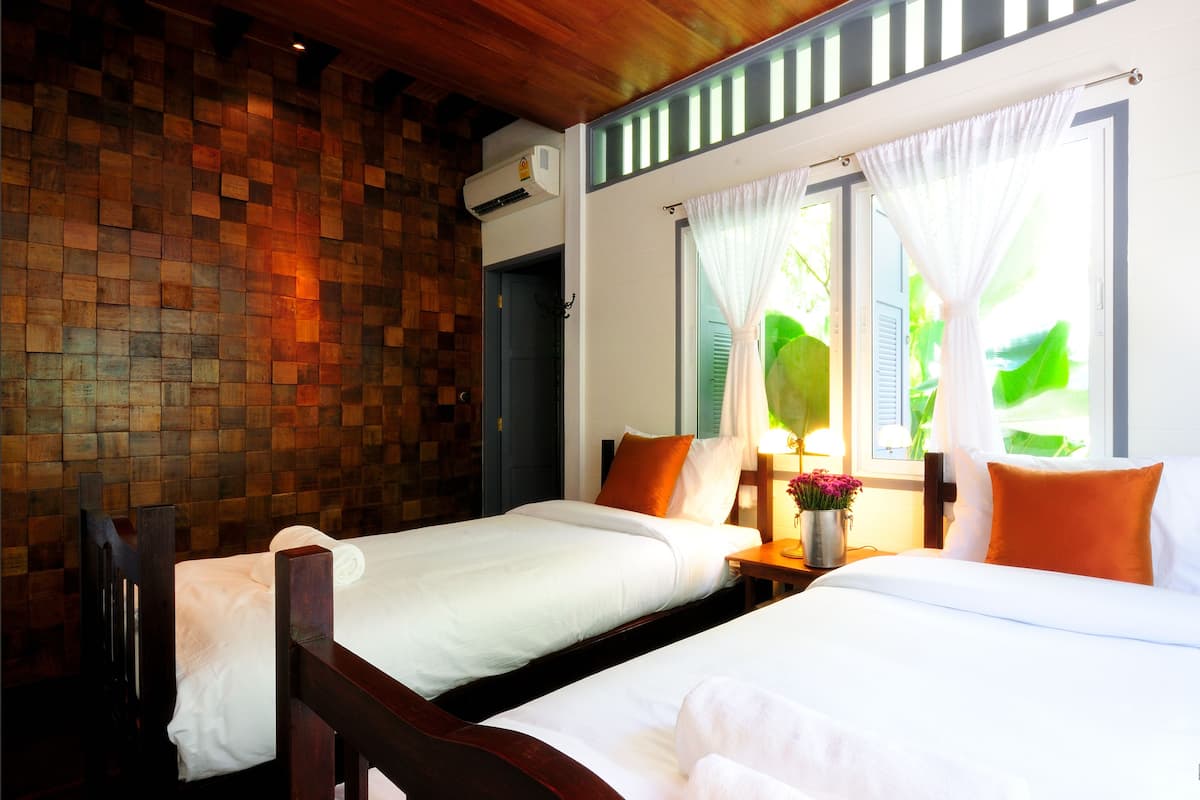 Une chambre d’hôtel avec deux lits, des murs en bois, une fenêtre avec des rideaux et une table de chevet avec une lampe et des fleurs.