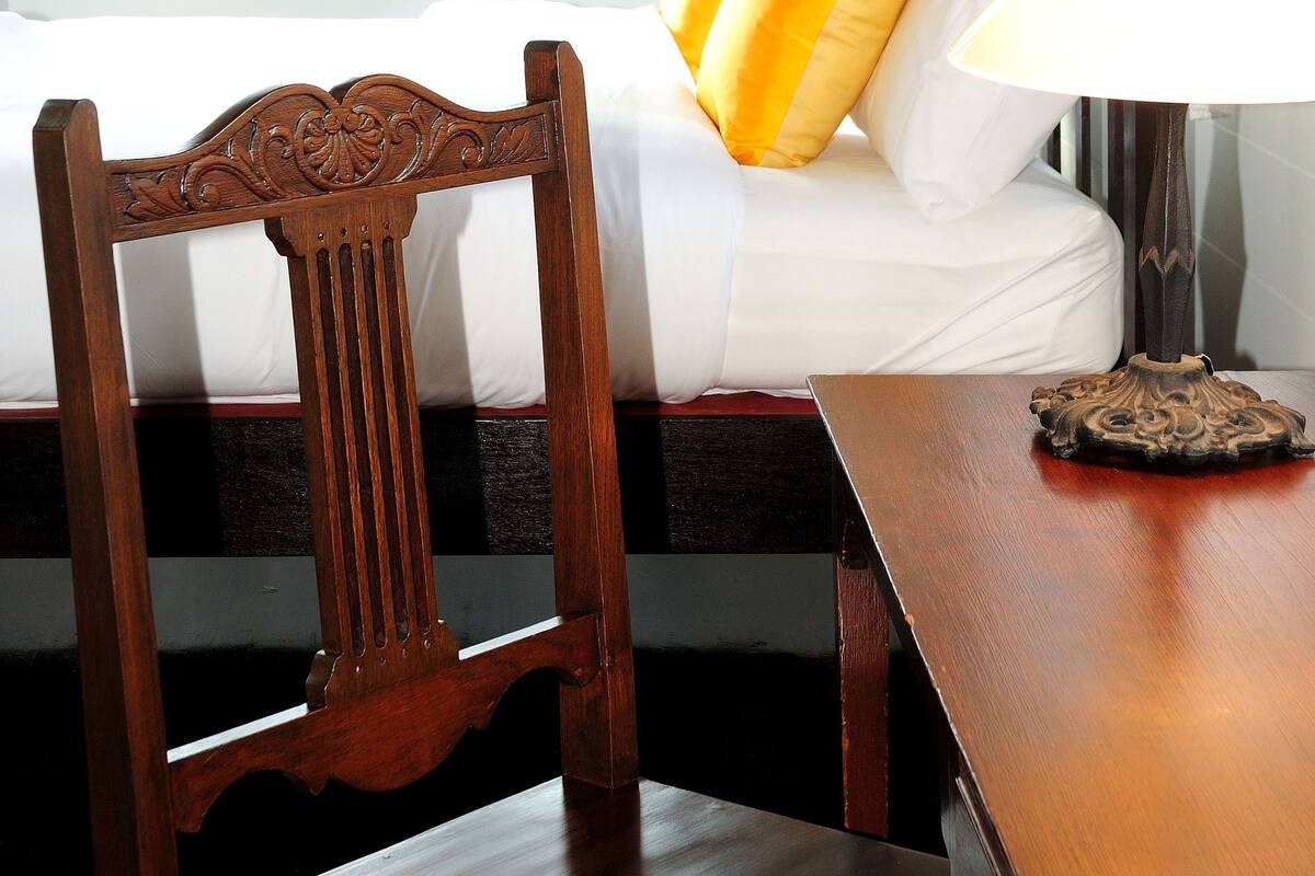 Une pièce comprenant un lit, une chaise en bois, une table et une fenêtre avec des rideaux.