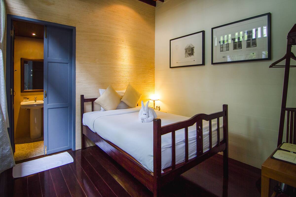 Une chambre à coucher avec un lit en bois, une table de chevet, une commode, un miroir et une porte donnant sur une salle de bain.