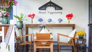 A wooden dining table with chairs, a sign above reading "Baan Noppawong," and various potted plants and flowers on the table. - Baan Noppawong (Bangkok)