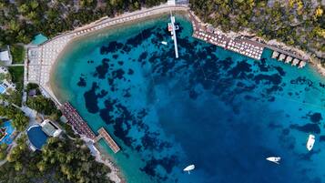 An aerial view of a coastal resort with a pier, beach umbrellas, and boats.