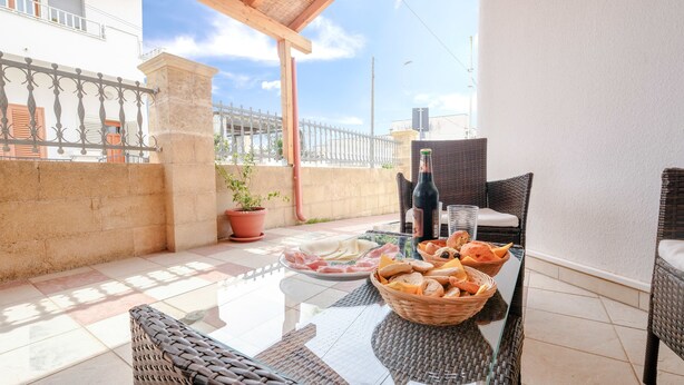 A patio with a glass table, wicker chairs, a potted plant, a bottle, and a basket of bread. - Casa Del Sole Relax Room (Castrignano del Capo)
