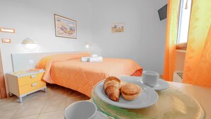A hotel room with a bed, a bedside table with a lamp, a small table with a plate of pastries, and a window with curtains. - Casa Del Sole Relax Room (Castrignano del Capo)