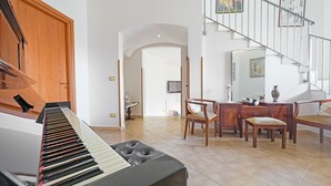A spacious living room with a piano, wooden furniture, a staircase, and a TV mounted on the wall. - Casa Del Sole Relax Room (Castrignano del Capo)
