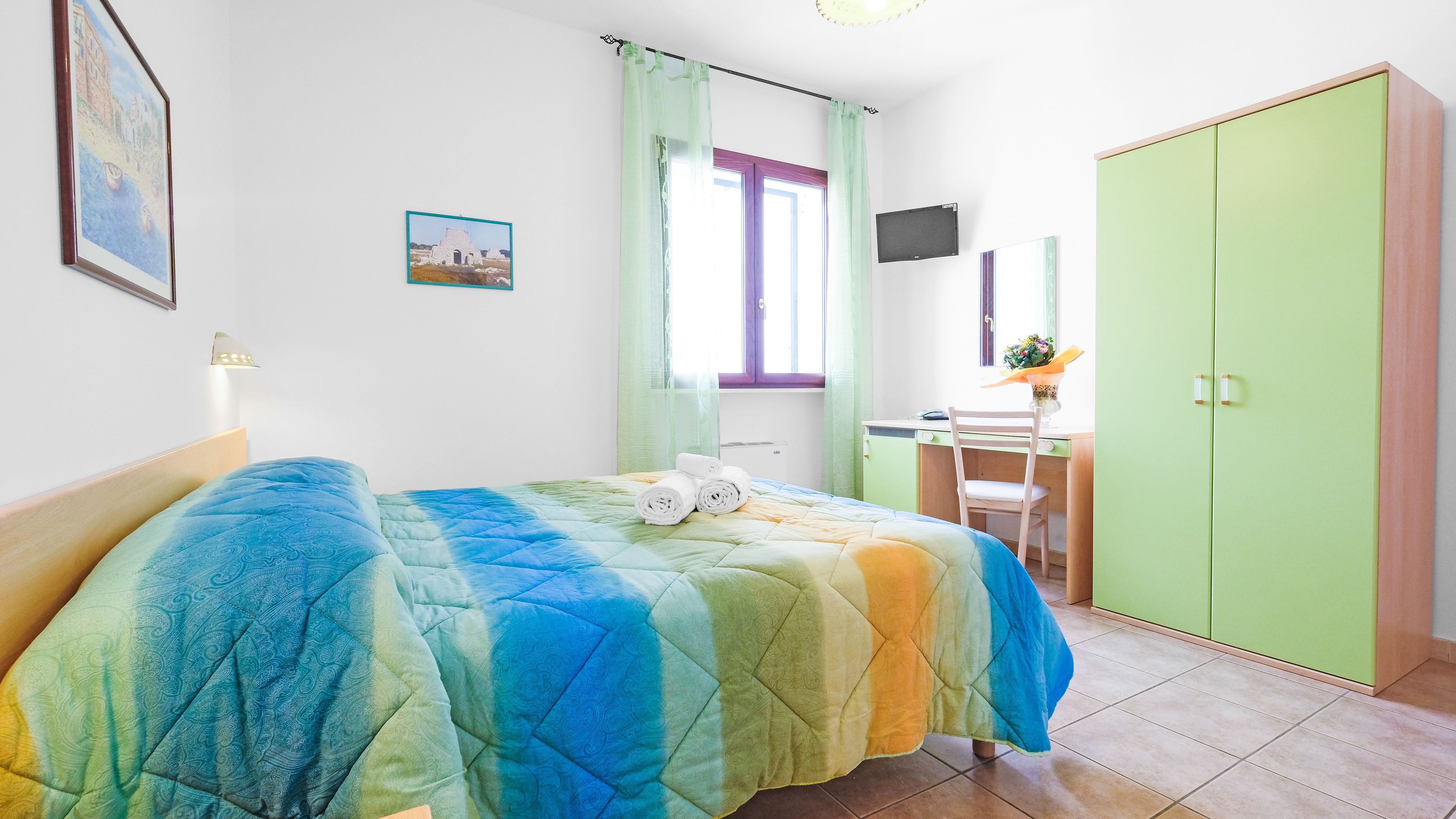 Une chambre à coucher comprenant un lit, un bureau, une chaise, une armoire et une fenêtre avec des rideaux.