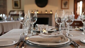 Una mesa de comedor dispuesta con varias copas de vino, platos y cubiertos, con una vela encendida en el centro.