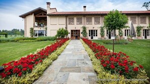 Un edificio grande de dos plantas con fachada simétrica, entrada central y un jardín bien cuidado con flores rojas y un camino de piedra.