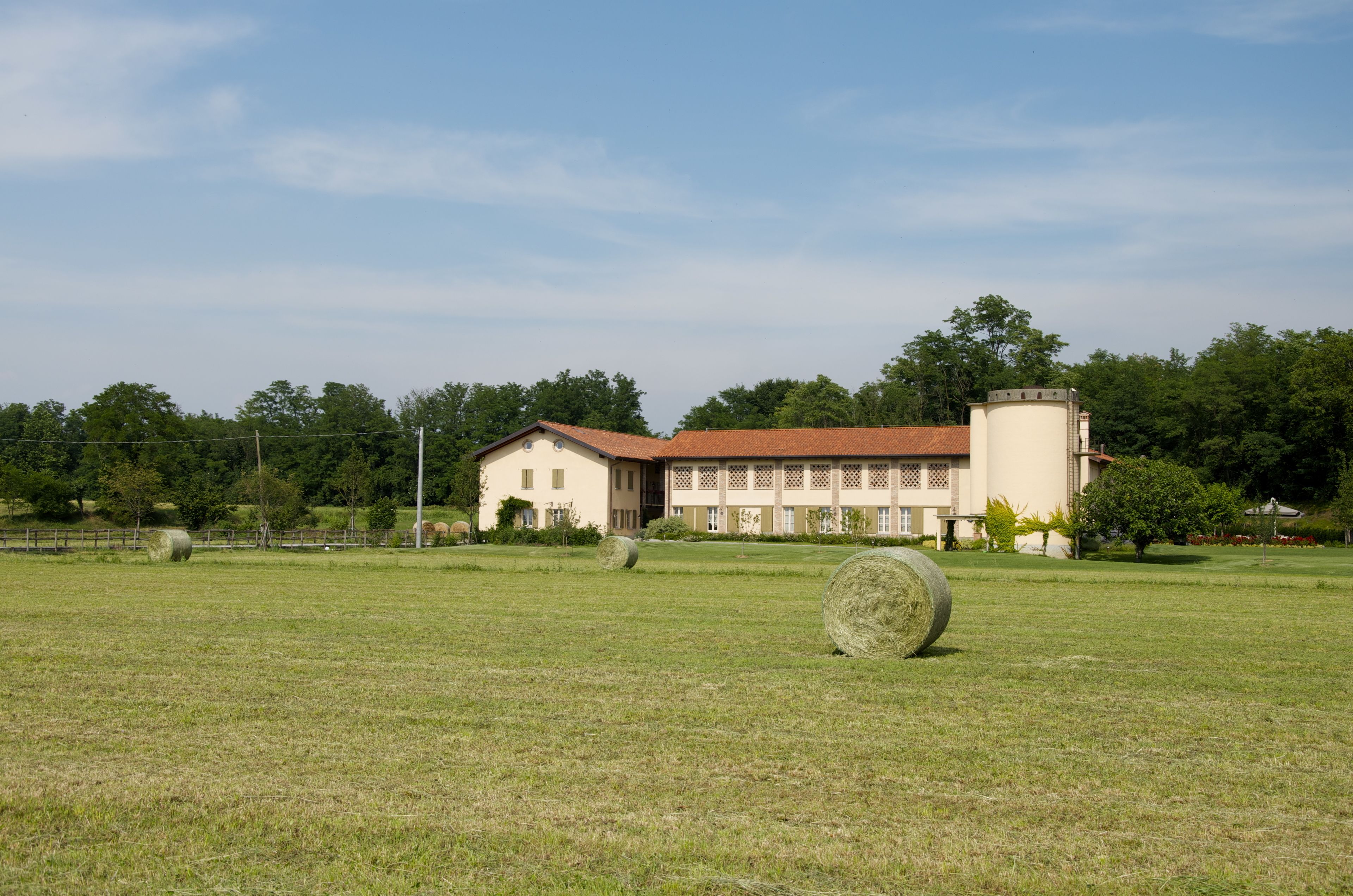 Ein großes Gebäude mit rotem Dach und beigen Wänden, umgeben von einem grasbewachsen Feld mit Heuballen.
