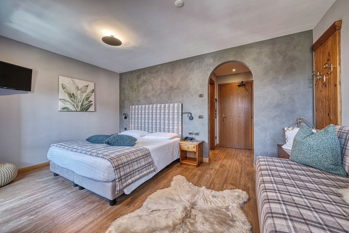 Ein Schlafzimmer mit zwei Betten, einem Holzschrank, einem kleinen Nachttisch, einem Wand-Fernseher und einer großen Pflanze.