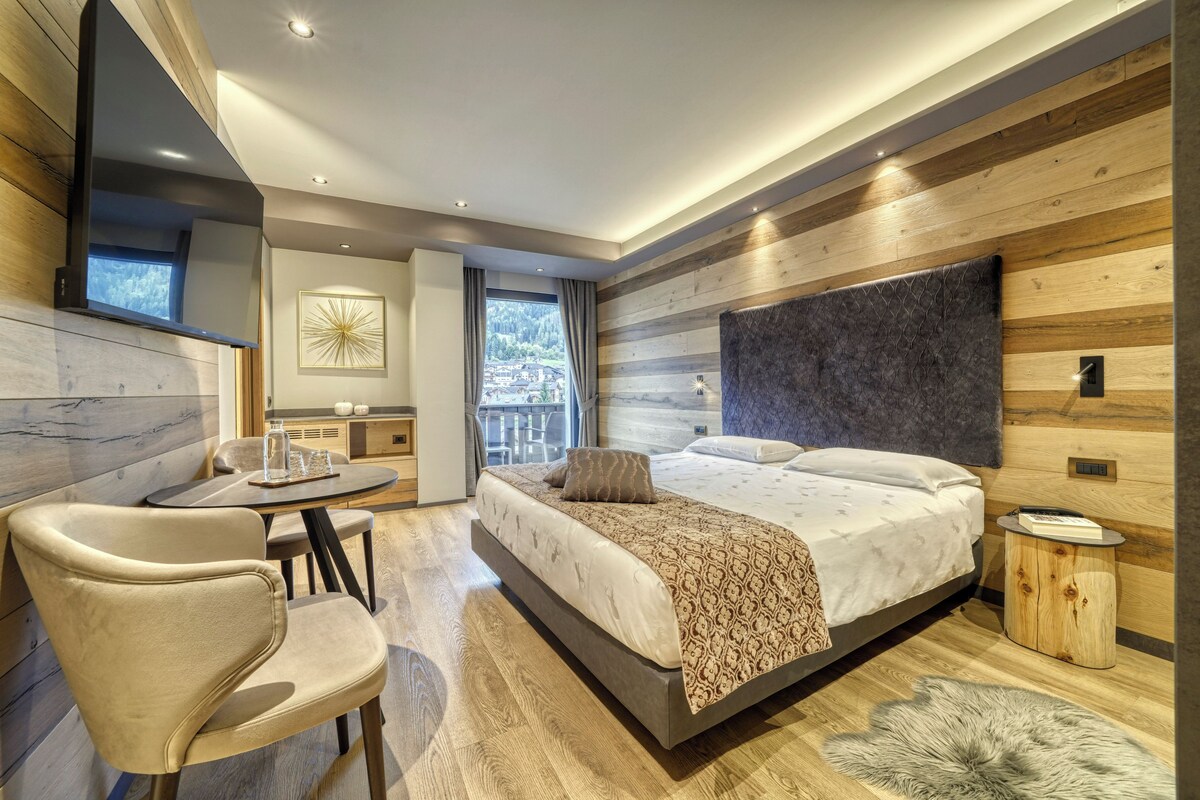 A modern bedroom with a large bed, a desk, and a view of the outdoors.