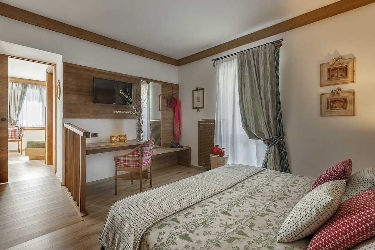Ein Schlafzimmer mit einem Holztisch, einem Bett mit gemusterten Betttextilien und Blick auf einen Balkon.