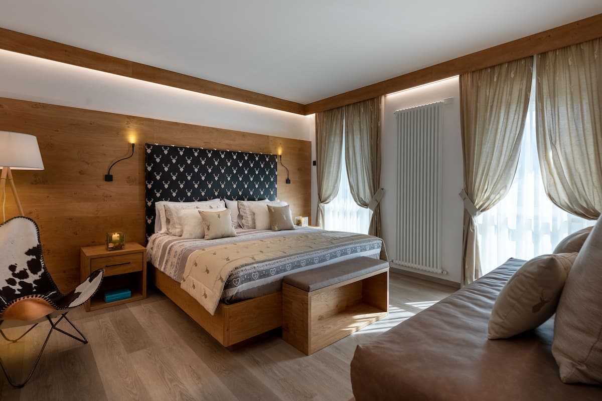 Ein modernes Schlafzimmer mit einem hölzernen Kopfteil, einem großen Bett mit gemustertem Bettbezug, einem Nachttisch mit Lampe, einem Sessel und einer Couch.