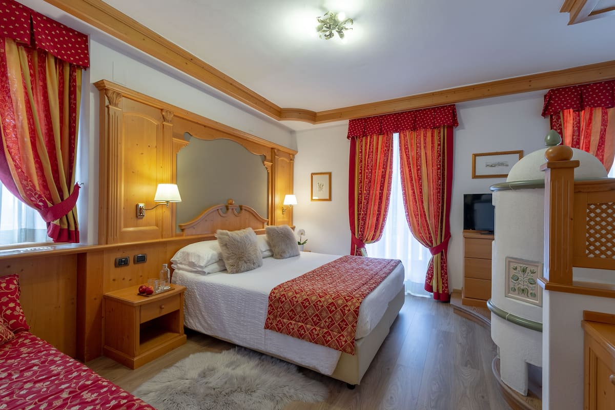 Ein Schlafzimmer mit Holz-Kopfteil, einem Bett mit weißer Bettwäsche und einer roten, gemusterten Tagesdecke, einem Nachttisch mit Lampe und einem großen Spiegel.