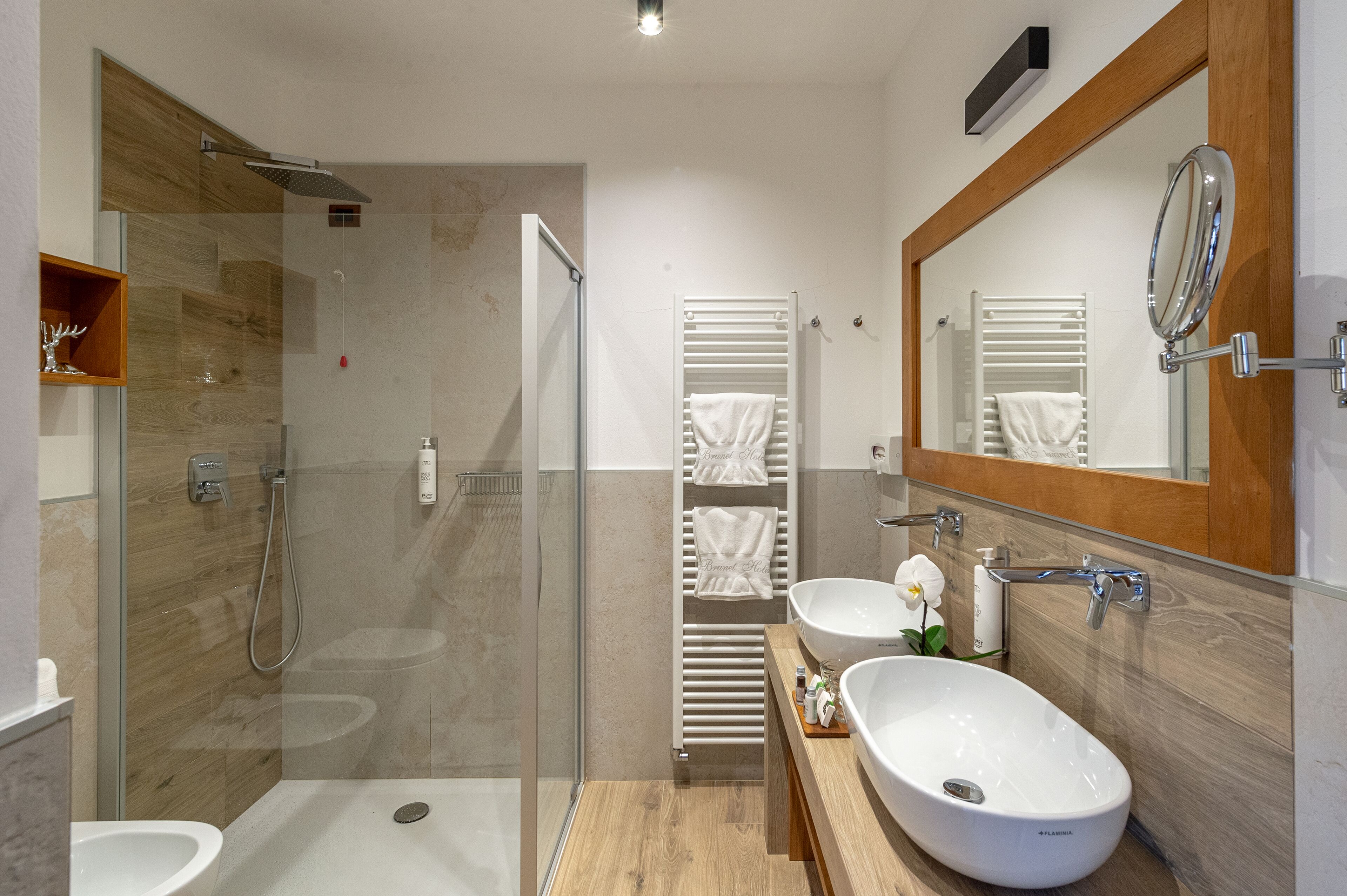 Ein modernes Badezimmer mit einer Duschkabine aus Glas, zwei Waschbecken und einem großen Spiegel.