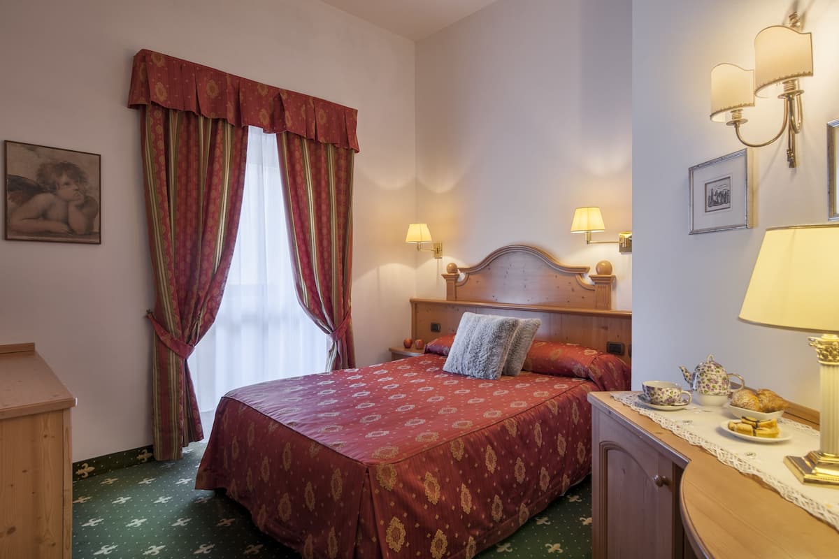 Ein Hotelzimmer mit einem großen Bett, einer Holzkommode, einem Nachttisch mit Lampe und einem Fenster mit Vorhängen.