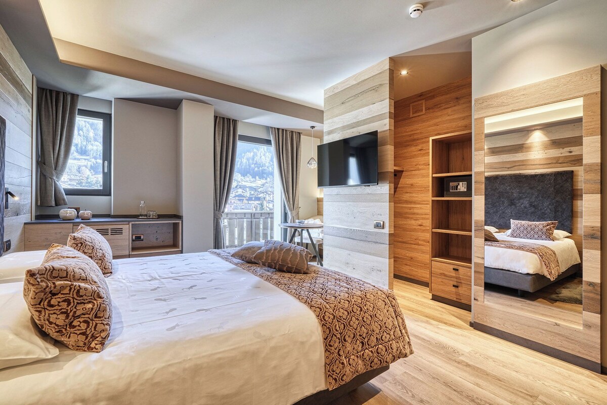 A modern bedroom with a large bed, a TV mounted on a wooden wall, and a built-in wardrobe.