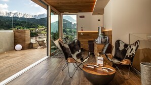 Un salon moderne doté d’un plafond en bois, de grandes fenêtres offrant une vue sur les montagnes, de fauteuils en cuir et d’une table en bois sur laquelle sont posés des magazines.