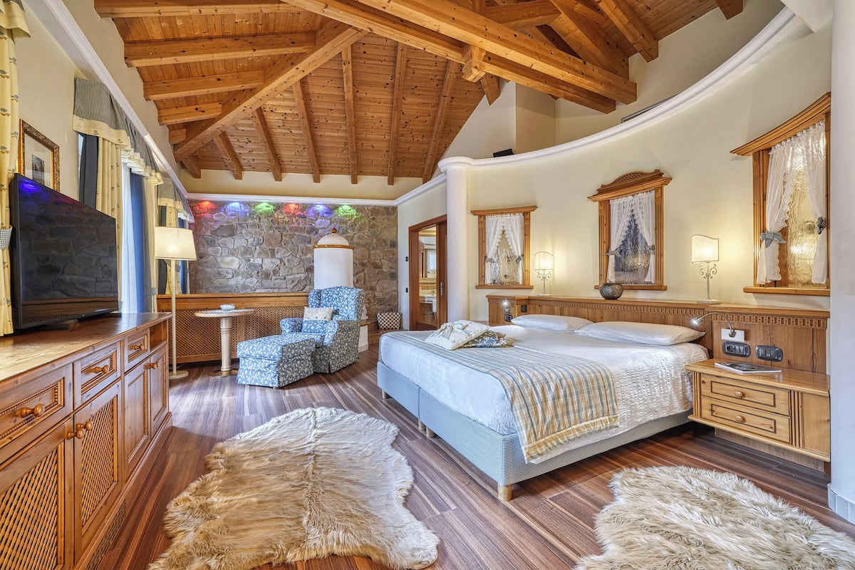 Ein geräumiges Schlafzimmer mit einem großen Bett, Holzbalkendecke, Steinwand und Kaminofen.