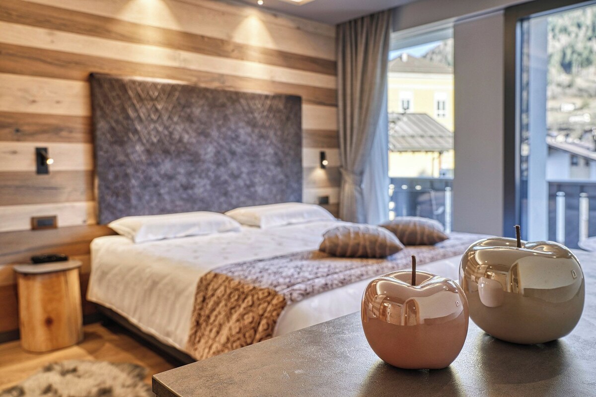 A modern hotel room with a large bed, a wooden headboard, and a view of a mountain.