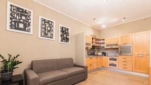 Un salon moderne avec un canapé, une petite table sur laquelle est posée une plante en pot, et une cuisine dotée de meubles et d’appareils électroménagers en bois.